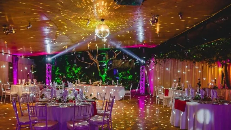 Fiesta con iluminación de colores sobre la pista de baile y mesas montadas alrededor
