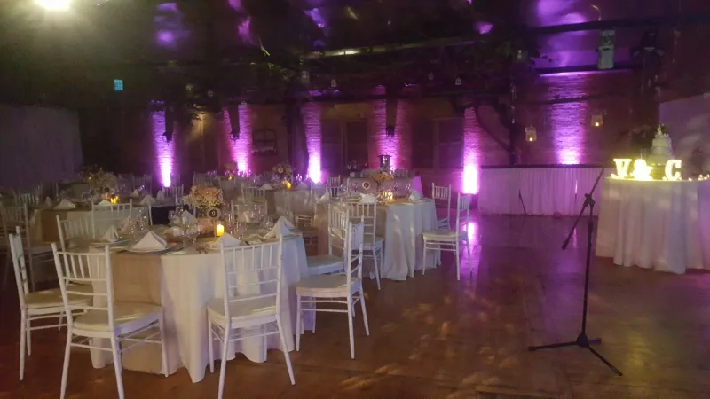 Salón de matrimonio con iluminación lila, mesas de banquete y letras iluminadas de los novios